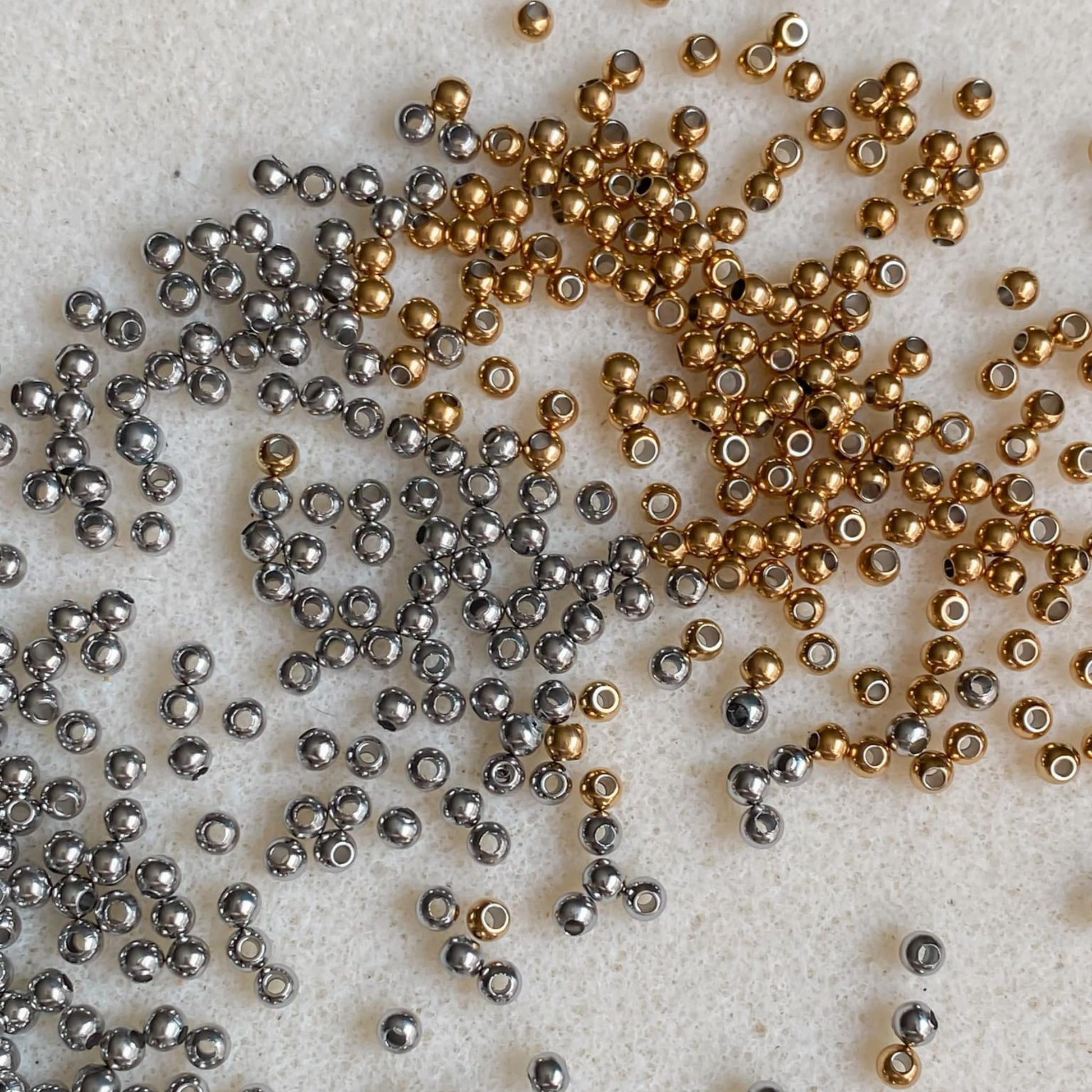 Billes en acier inoxydable doré et argenté montrant les différentes finitions disponibles pour les bracelets cordon personnalisables, illustrant les choix de couleur pour le design.