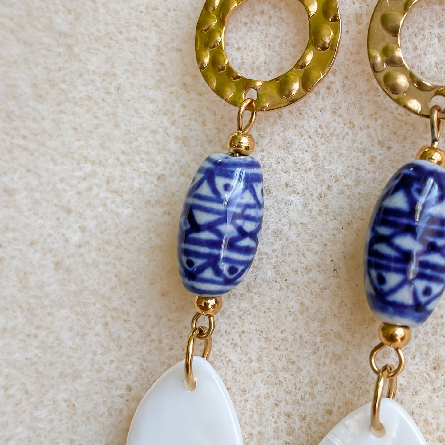 Détail des boucles d’oreilles Abalone en acier inoxydable doré avec perle en céramique bleue et nacre en forme de goutte.