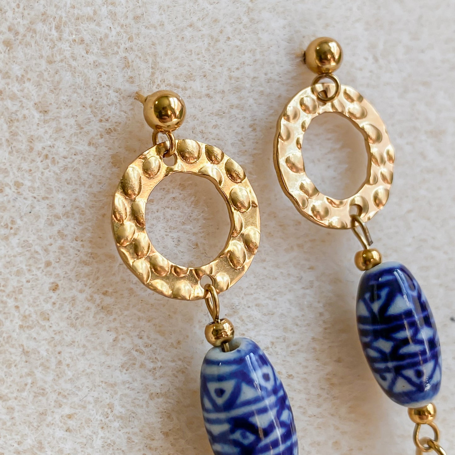 Gros plan sur les boucles d’oreilles Abalone avec cercle doré texturé et perle ovale en céramique bleue.