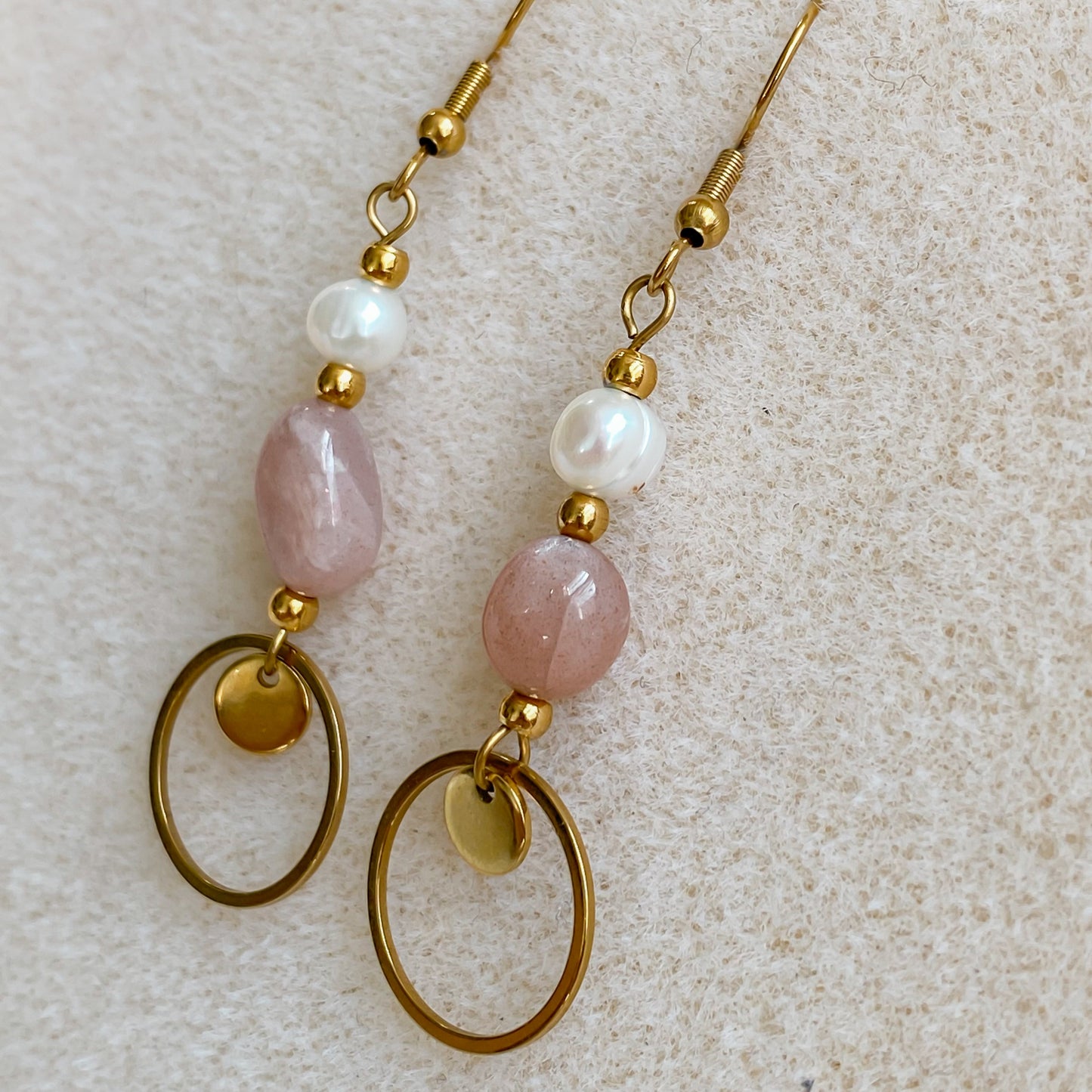 Boucles pendantes Daphné en plaqué or, perle d’eau douce et pierre de soleil, vues en gros plan sur fond beige granuleux