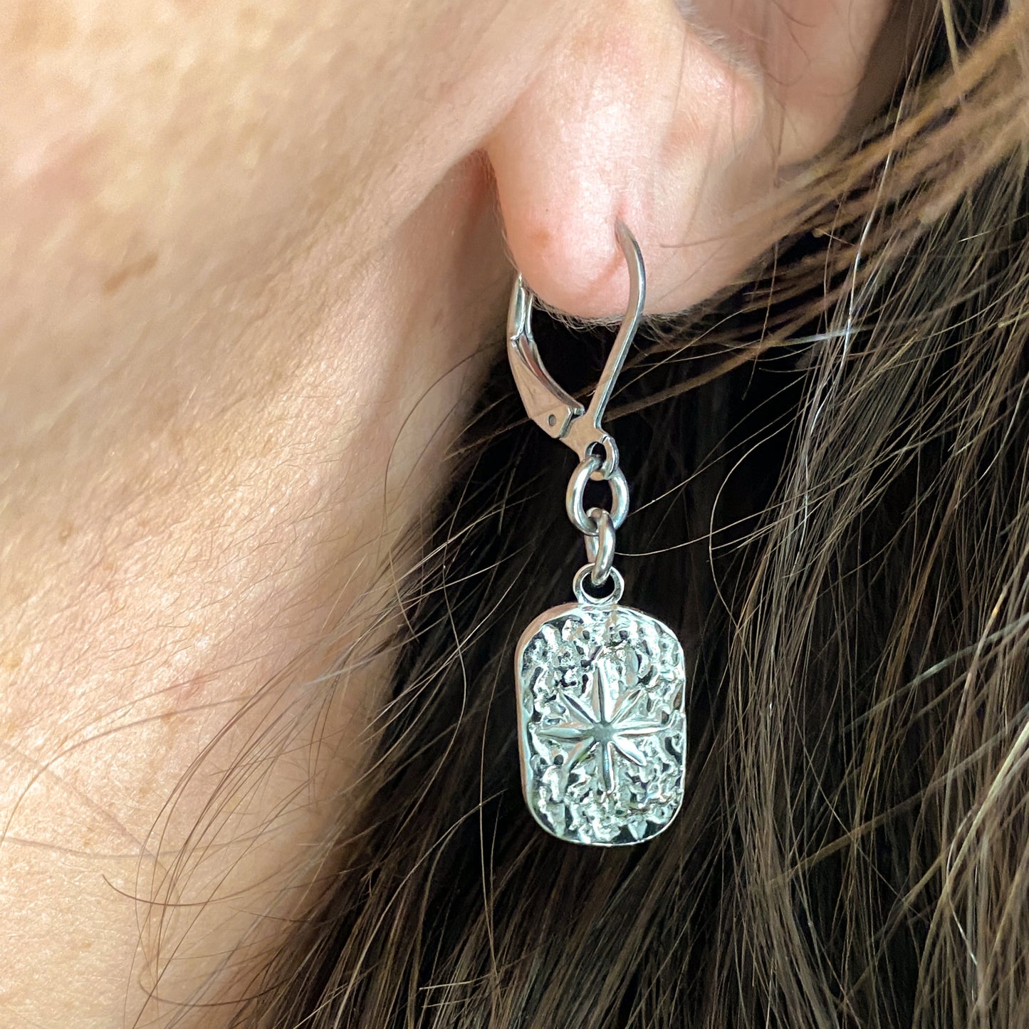 Gros plan d’une boucle d’oreille Estrella en acier inoxydable argenté portée à l’oreille – pendentif étoile texturé