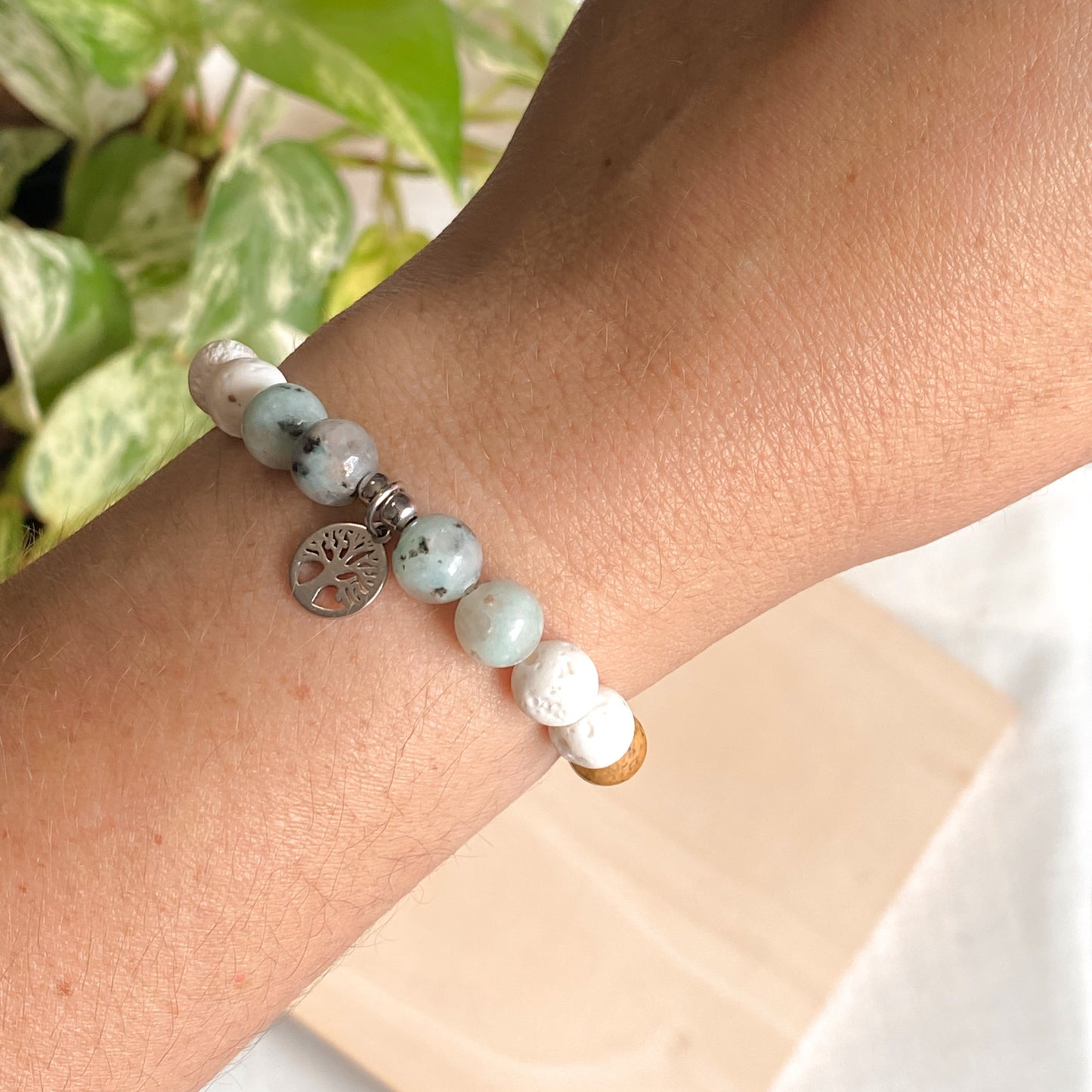 Bracelet arbre de vie en jaspe kiwi, jaspe paysage et lave blanche porté sur une main féminine, pendentif arbre argenté.