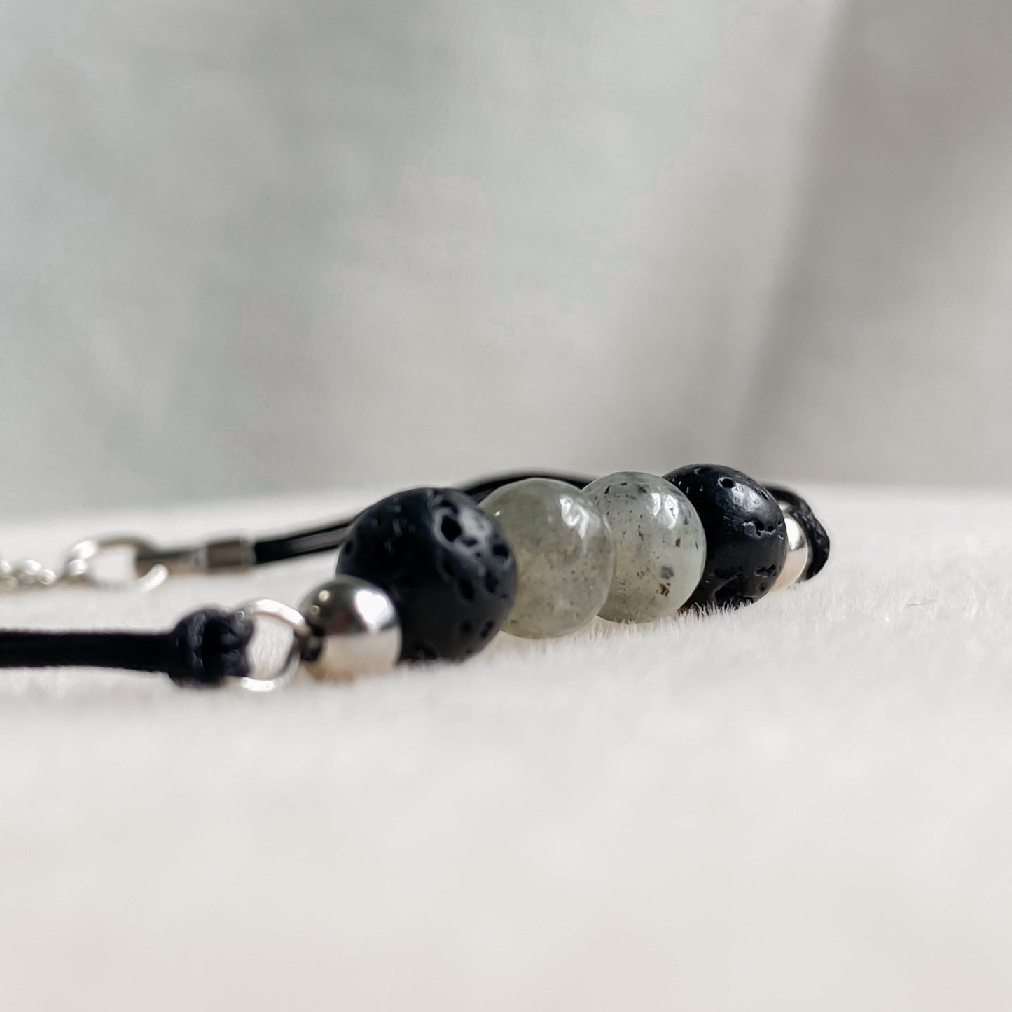 Gros plan sur un bracelet artisanal en pierres de lave et labradorite de 6 mm, monté sur cordon noir avec détails en acier inoxydable.