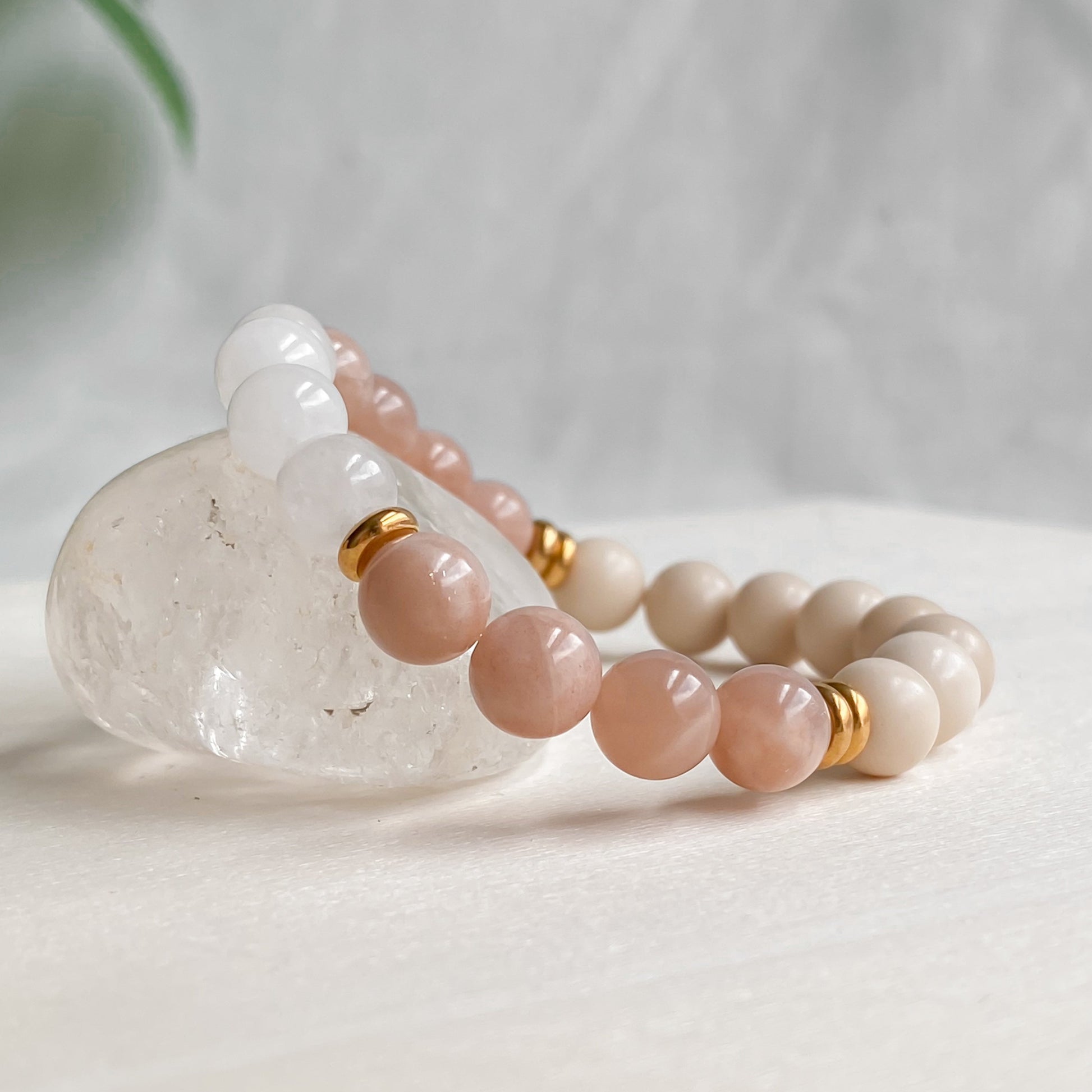 Gros plan du bracelet Éclat de Soleil en pierres semi-précieuses (pierre de soleil, pierre de rivière, quartz blanc) et acier inoxydable doré, mettant en valeur les reflets de la pierre de soleil, posé sur une pierre brute de quartz clair dans une assiette blanche avec une lumière naturelle douce.