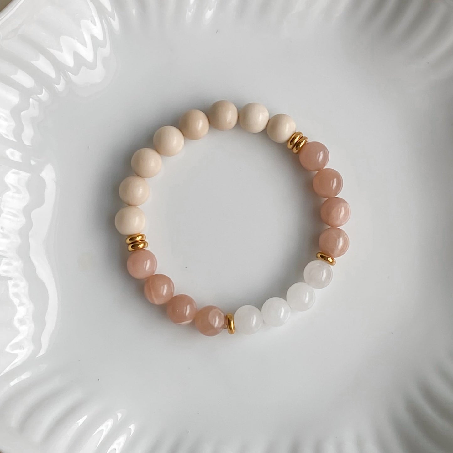 Bracelet élastique Éclat de Soleil en pierre de soleil, pierre de rivière et quartz blanc (8mm) avec acier inoxydable doré, vu de haut, posé dans une assiette blanche.