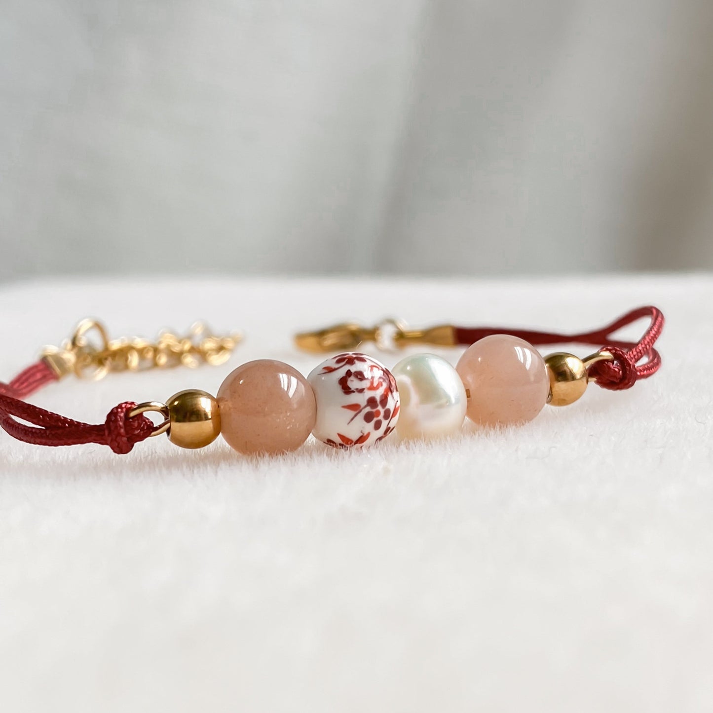 Gros plan sur les perles du bracelet Éveil, cordon rouge en pierres naturelles avec pierre de soleil, perle d’eau douce et perle en céramique décorée.