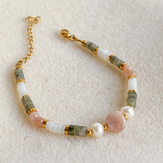 Bracelet Hécate en pierres naturelles avec pierre de soleil, jade blanc, labradorite et perle d’eau douce, sur fond beige.