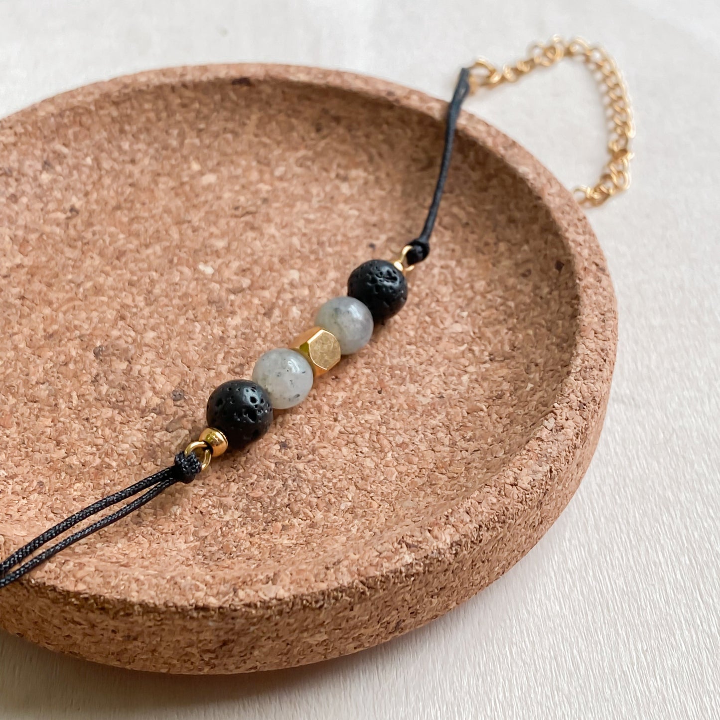 Bracelet cadeau bien-être NOCTIS, cordon noir et perles de lave diffuseuses, avec labradorite et détails dorés en acier inoxydable.