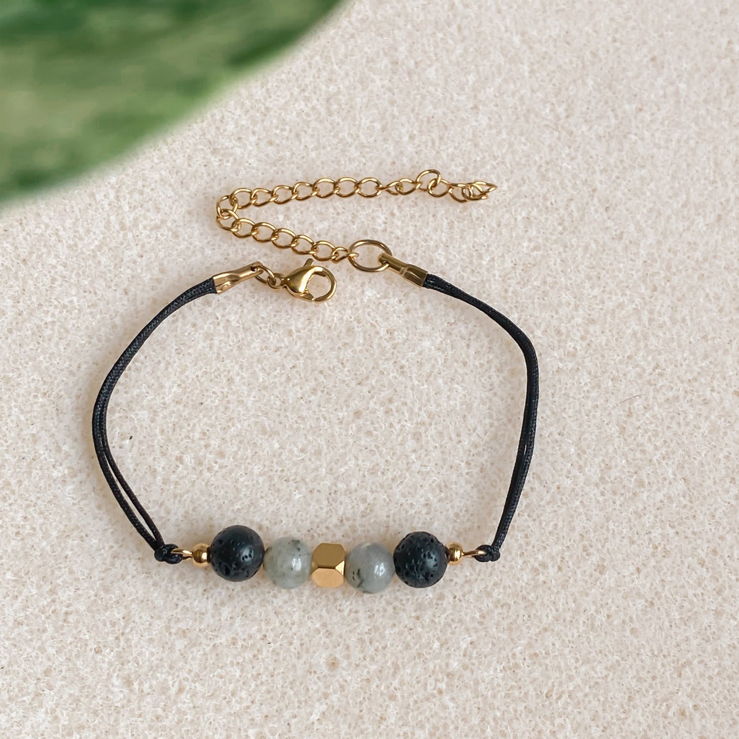 Bracelet cordon ajustable NOCTIS en pierres naturelles, diffuseur d’huiles essentielles, posé à plat avec fermoir doré visible.