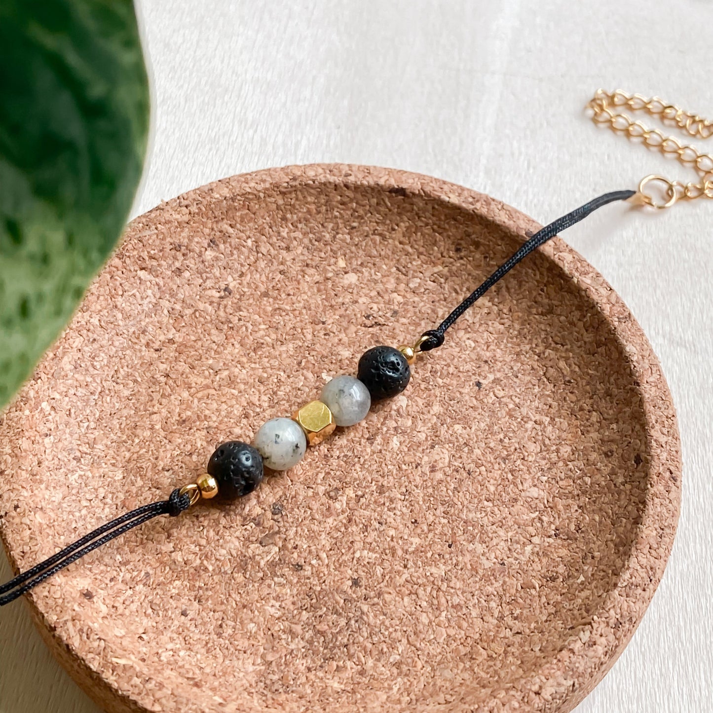 Bracelet artisanal NOCTIS diffuseur d’aromathérapie, cordon noir et pierres naturelles, présenté sur support rond en liège.