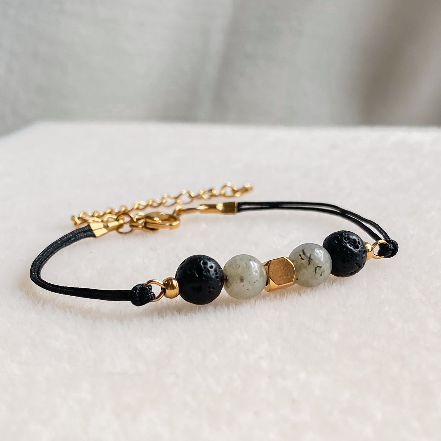 Bracelet NOCTIS en cordon noir avec pierres de lave et labradorite, diffuseur d’huiles essentielles, vue rapprochée sur fond clair.
