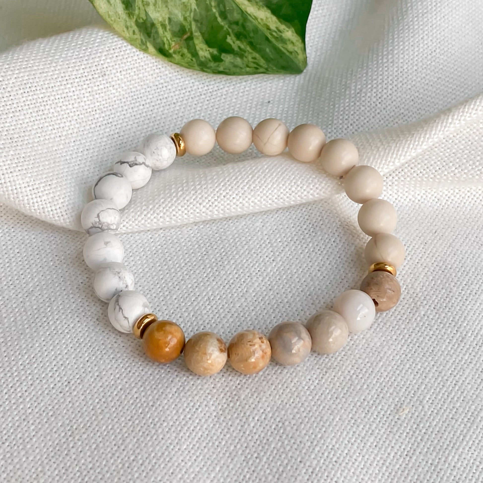 Gros plan du bracelet Renouveau en pierres naturelles et acier inoxydable doré, capturant la texture et les nuances des pierres, posé sur une nappe en coton naturel entouré de plantes.