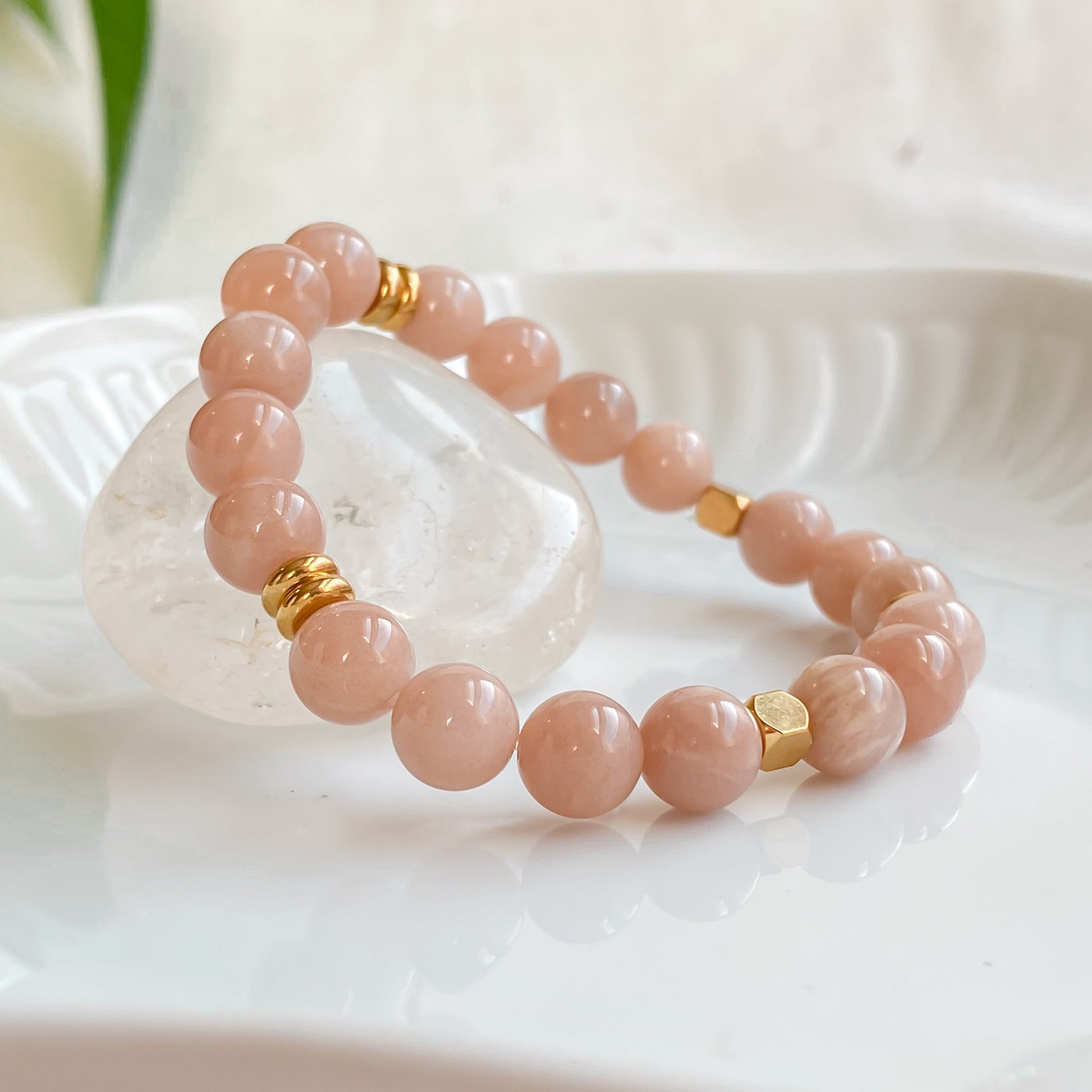 Gros plan du bracelet élastique Sparkles en pierre de soleil 8mm et acier inoxydable doré, posé sur une pierre brute de quartz clair dans une assiette blanche, avec une lumière naturelle douce.