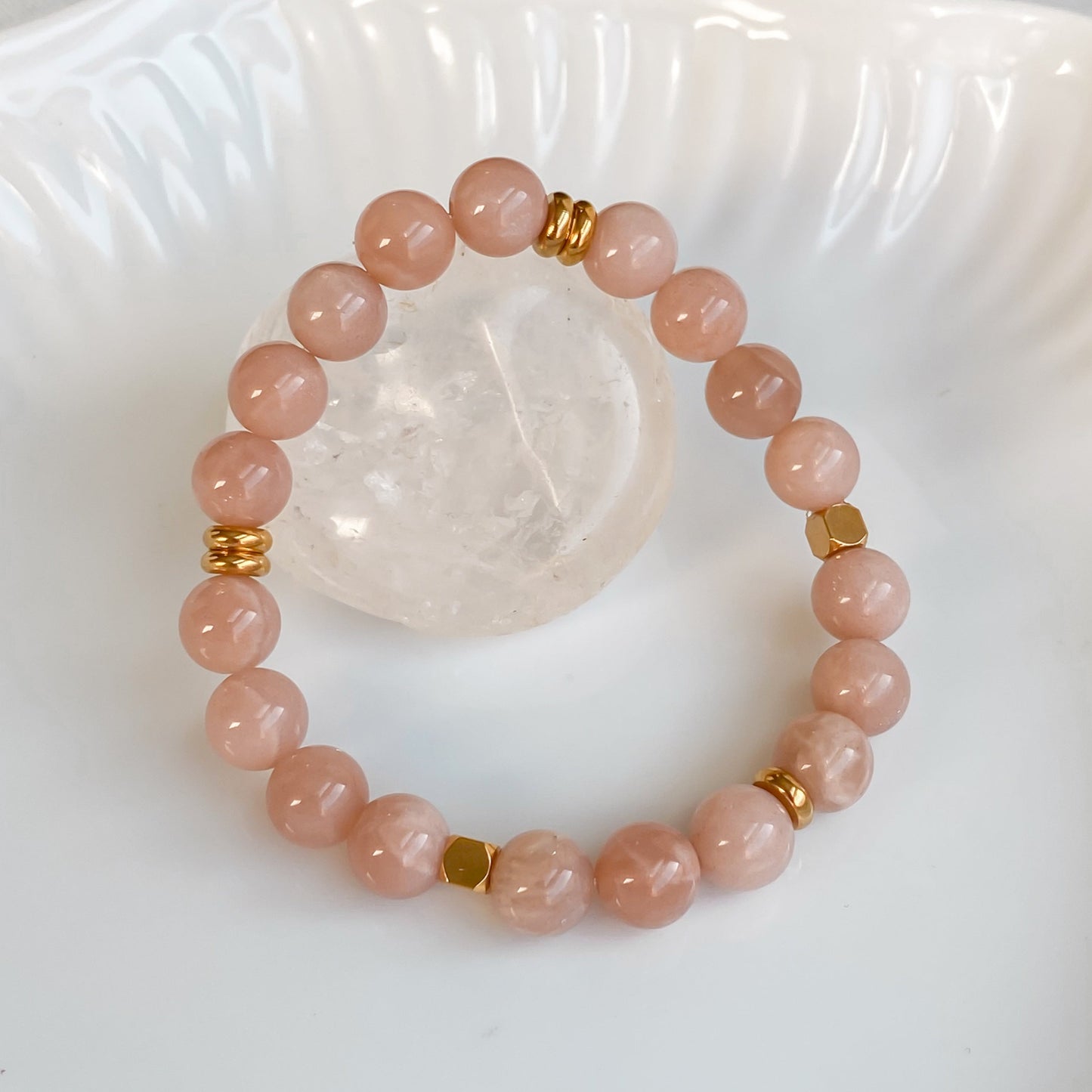 Bracelet élastique Sparkles en pierre de soleil et acier inoxydable doré vu de haut, disposé sur une pierre brute de quartz clair dans une assiette blanche, entouré de plantes sur une nappe en coton naturel.