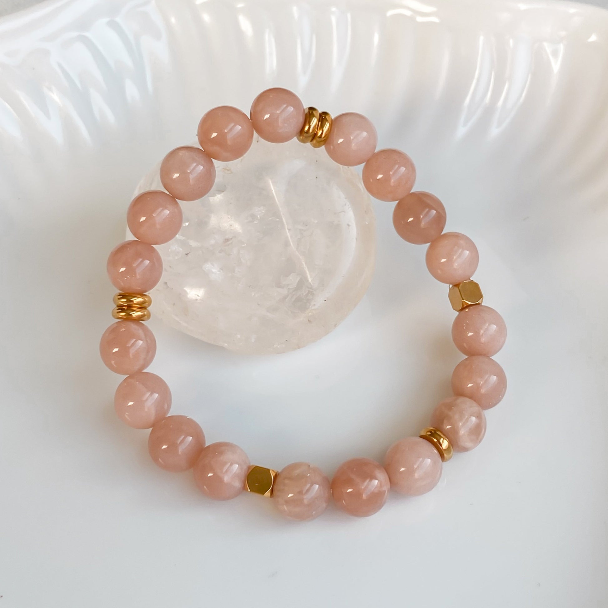 Bracelet élastique Sparkles en pierre de soleil et acier inoxydable doré vu de haut, disposé sur une pierre brute de quartz clair dans une assiette blanche, entouré de plantes sur une nappe en coton naturel.