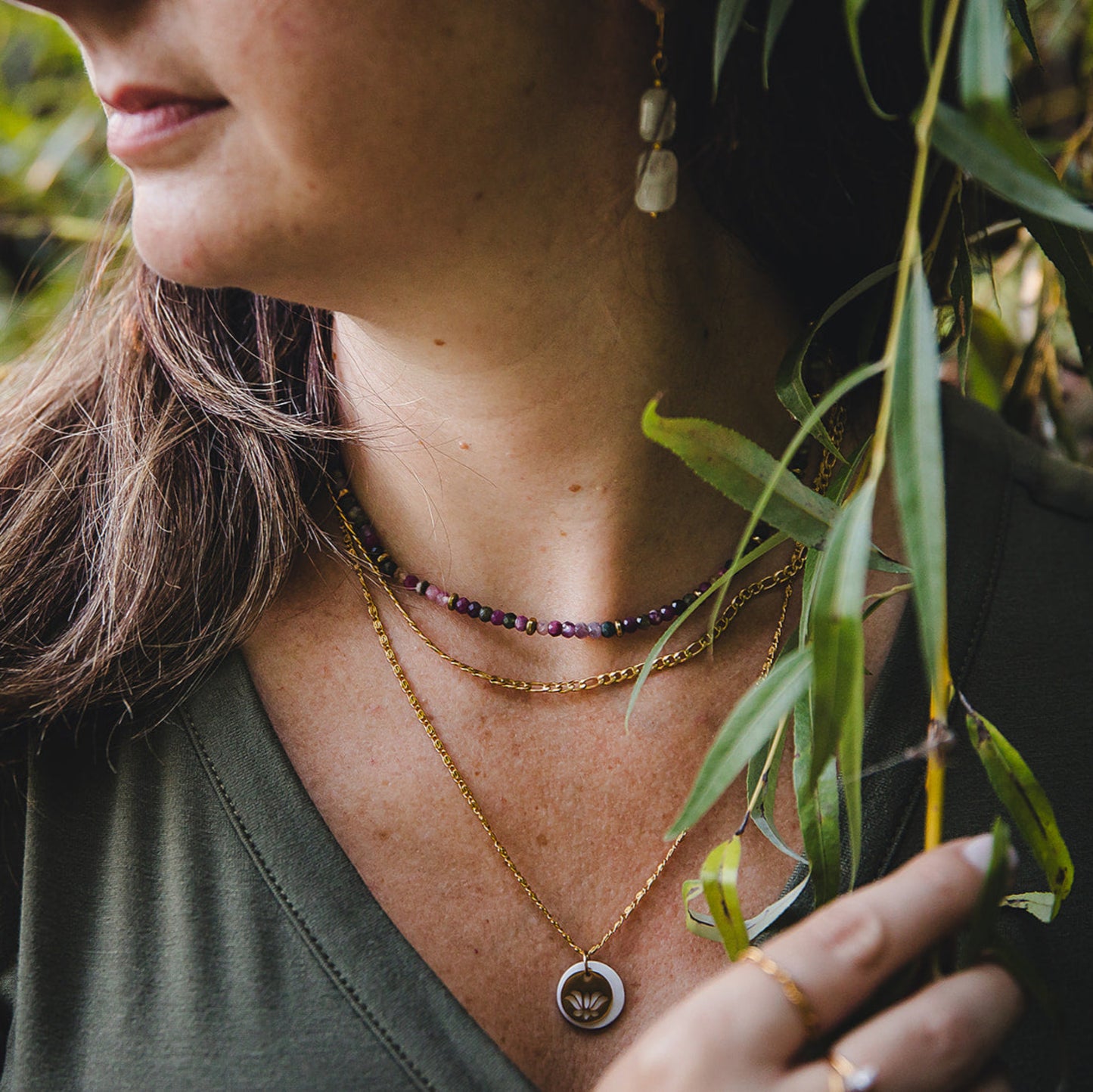Gros plan sur le collier Aurora en acier inoxydable doré 18K, superposé avec un collier de pierres naturelles et un pendentif doré, look bohème chic.