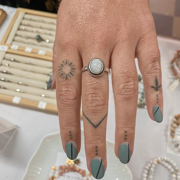 Bague Moonstone en Argent Sterling 925 portée sur le majeur par une cliente tatouée et manucurée, mettant en valeur la pierre de lune arc-en-ciel au centre, ajoutant une touche d'élégance et de mystère.