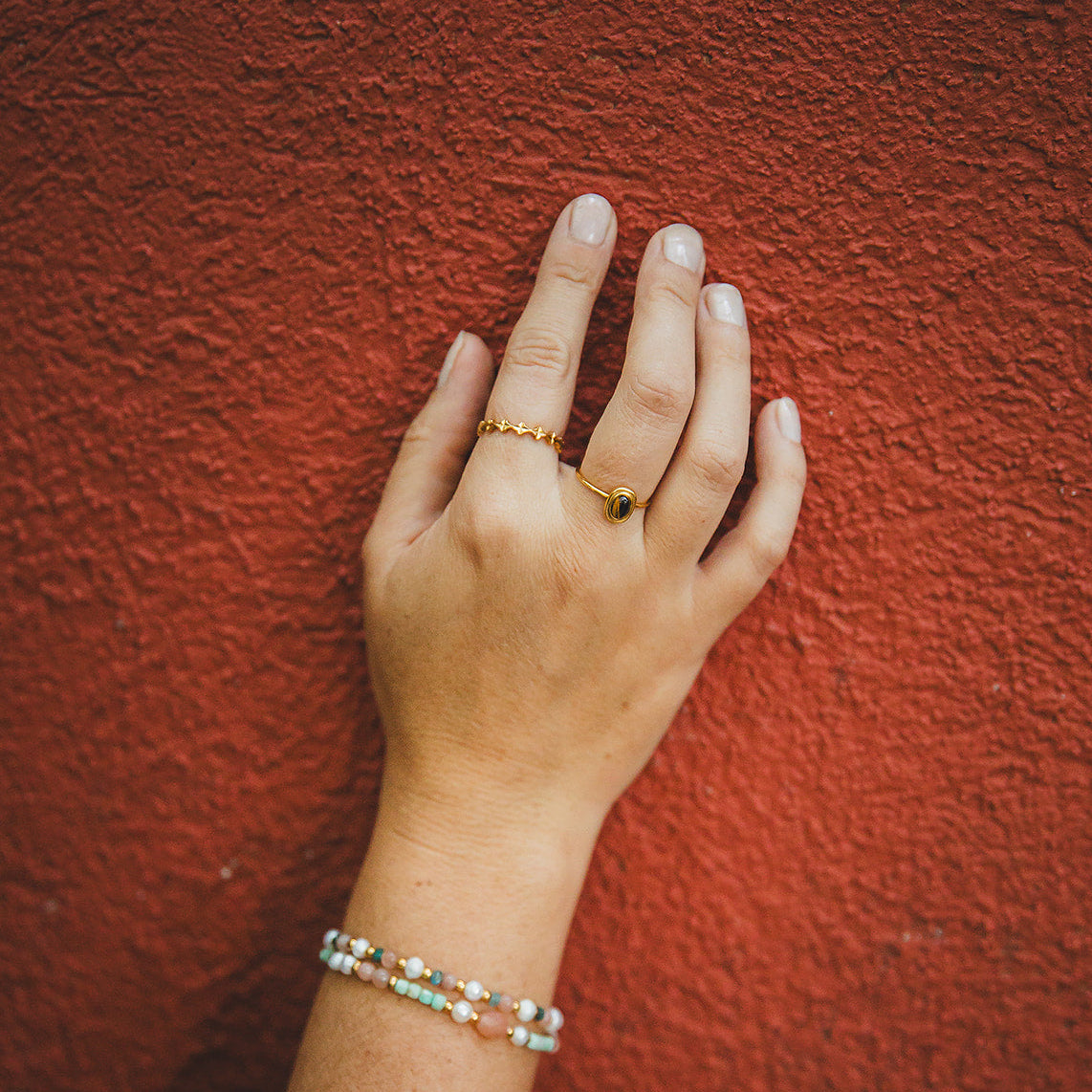 Bague Arabesque dorée portée devant un mur terracotta