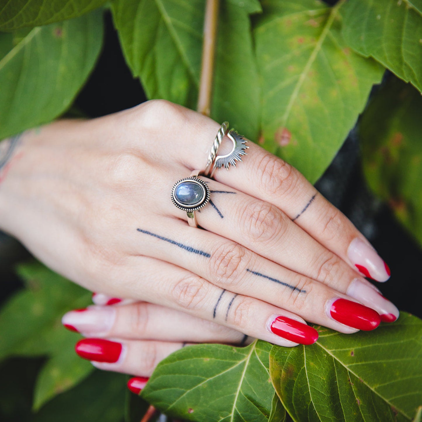 Bague Morgane en argent et labradorite portée à la main, photographiée dans un décor naturel avec feuilles vertes.