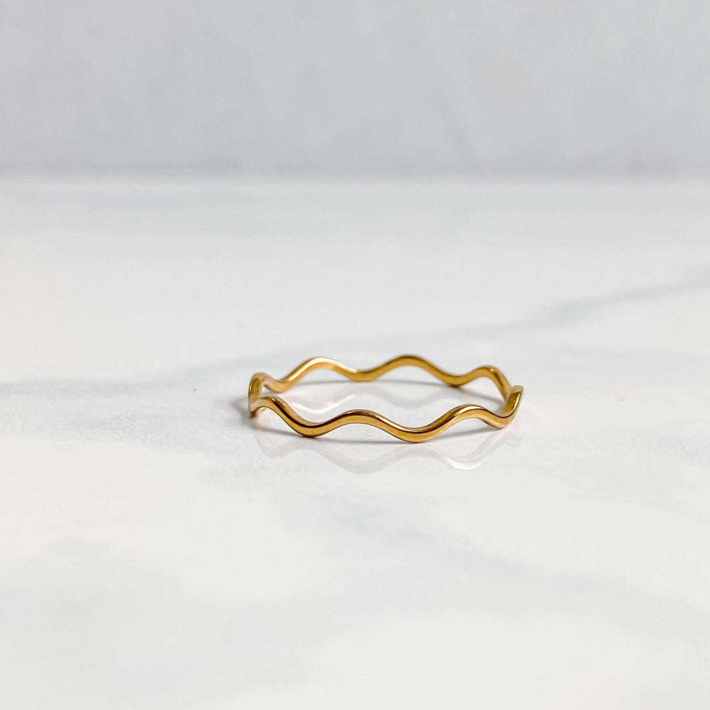 Bague Naïa ondulée dorée minimaliste posée sur une surface claire