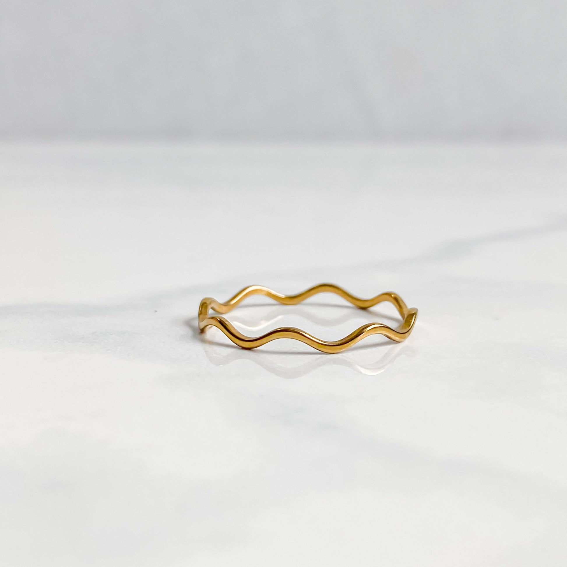 Bague Naïa ondulée dorée minimaliste posée sur une surface claire