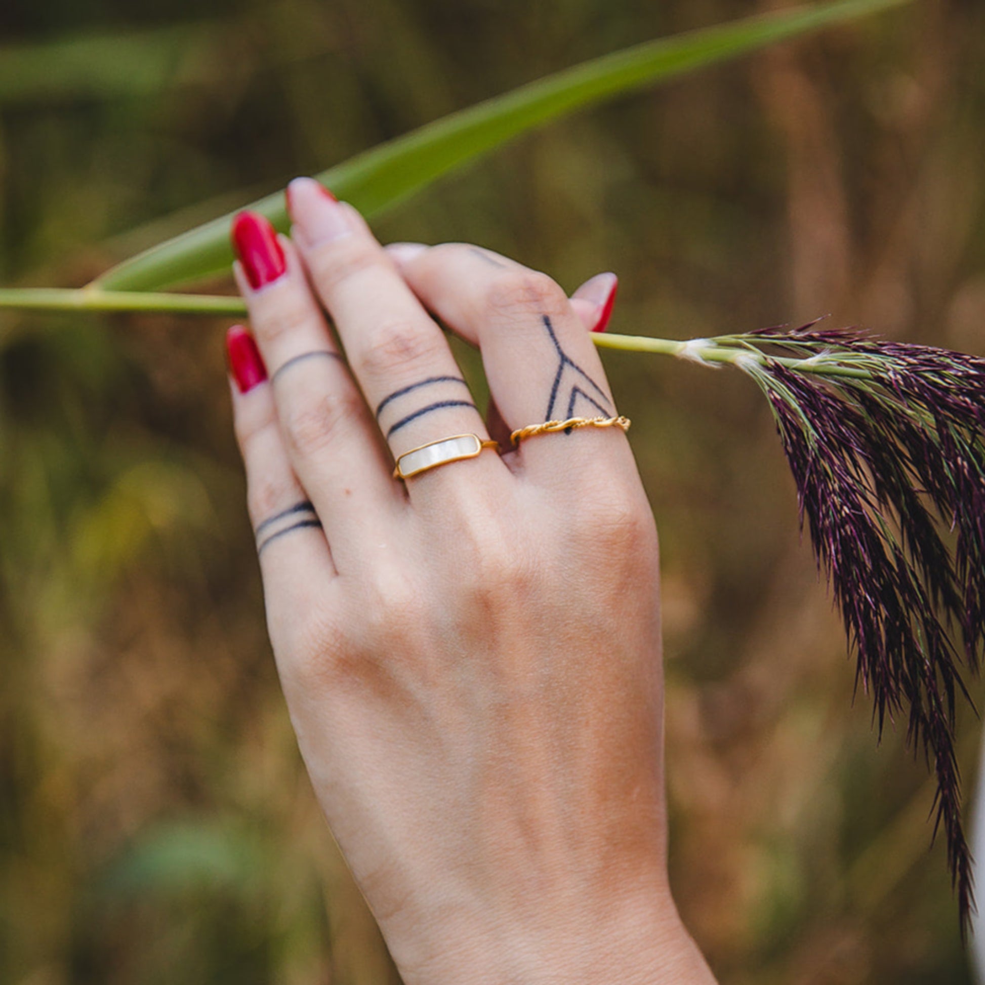 Bague Rhéa torsadée en acier inoxydable plaqué or 18K portée à la main, photo en extérieur avec bracelet perles naturelles.