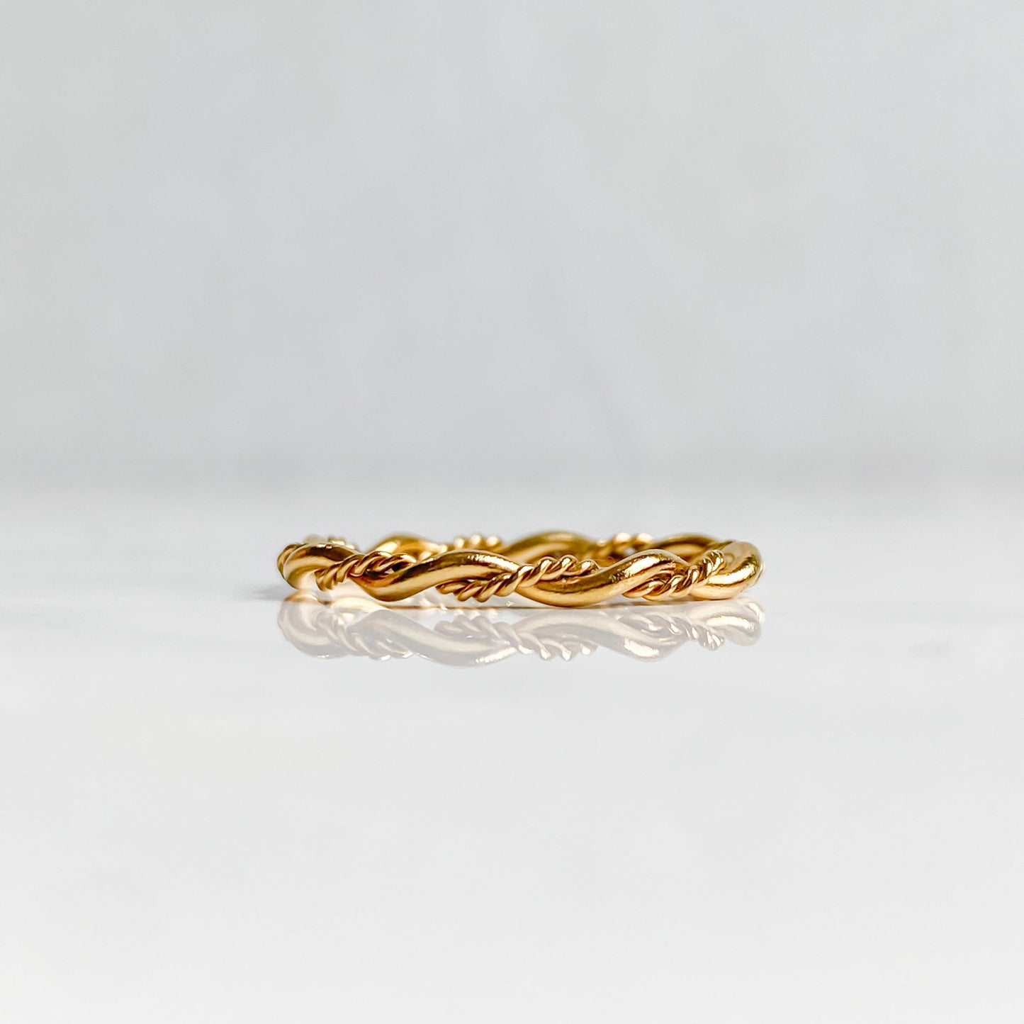 Bague Rhéa torsadée en acier inoxydable plaqué or 18K, vue de profil posée à plat.
