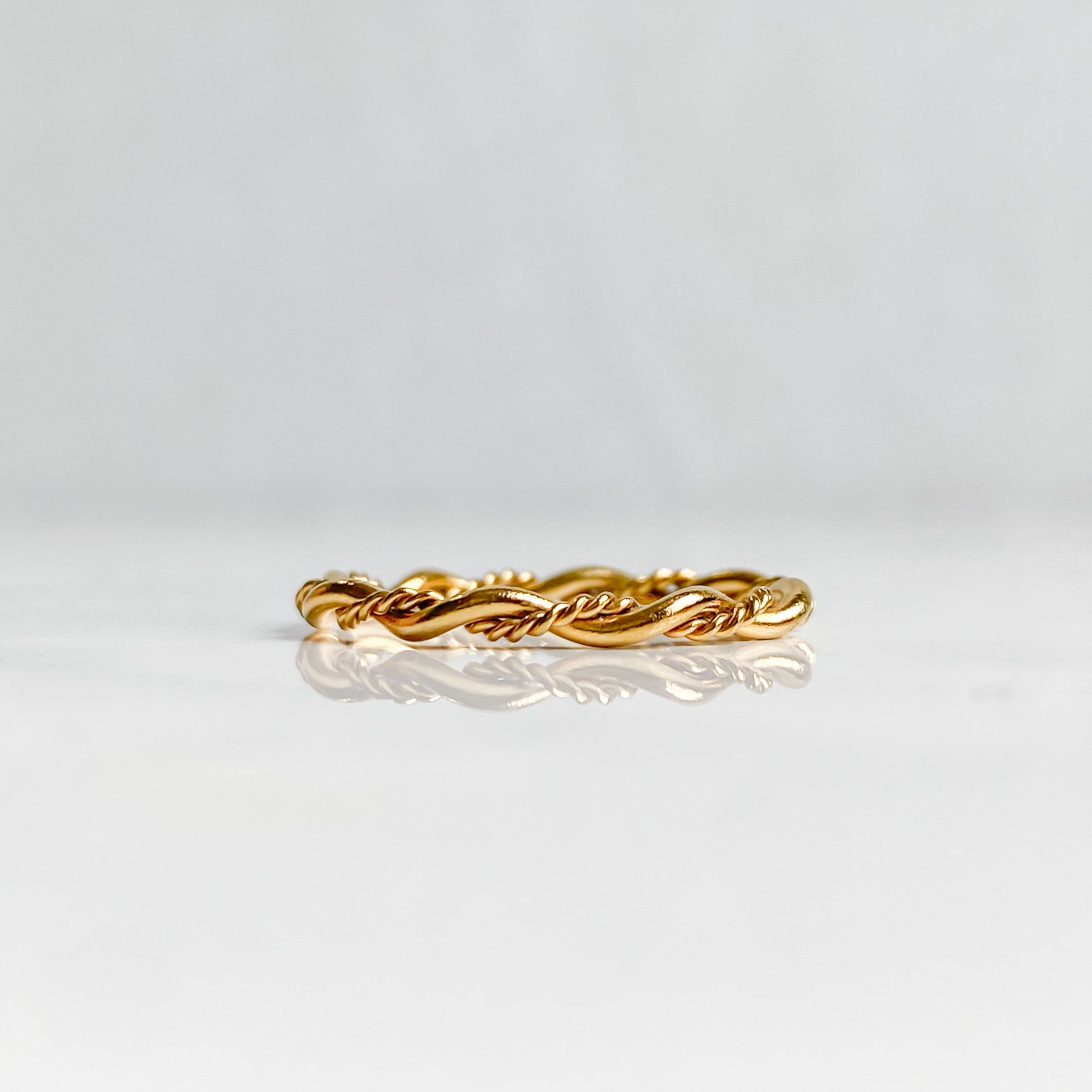 Bague Rhéa torsadée en acier inoxydable plaqué or 18K, vue de profil posée à plat.
