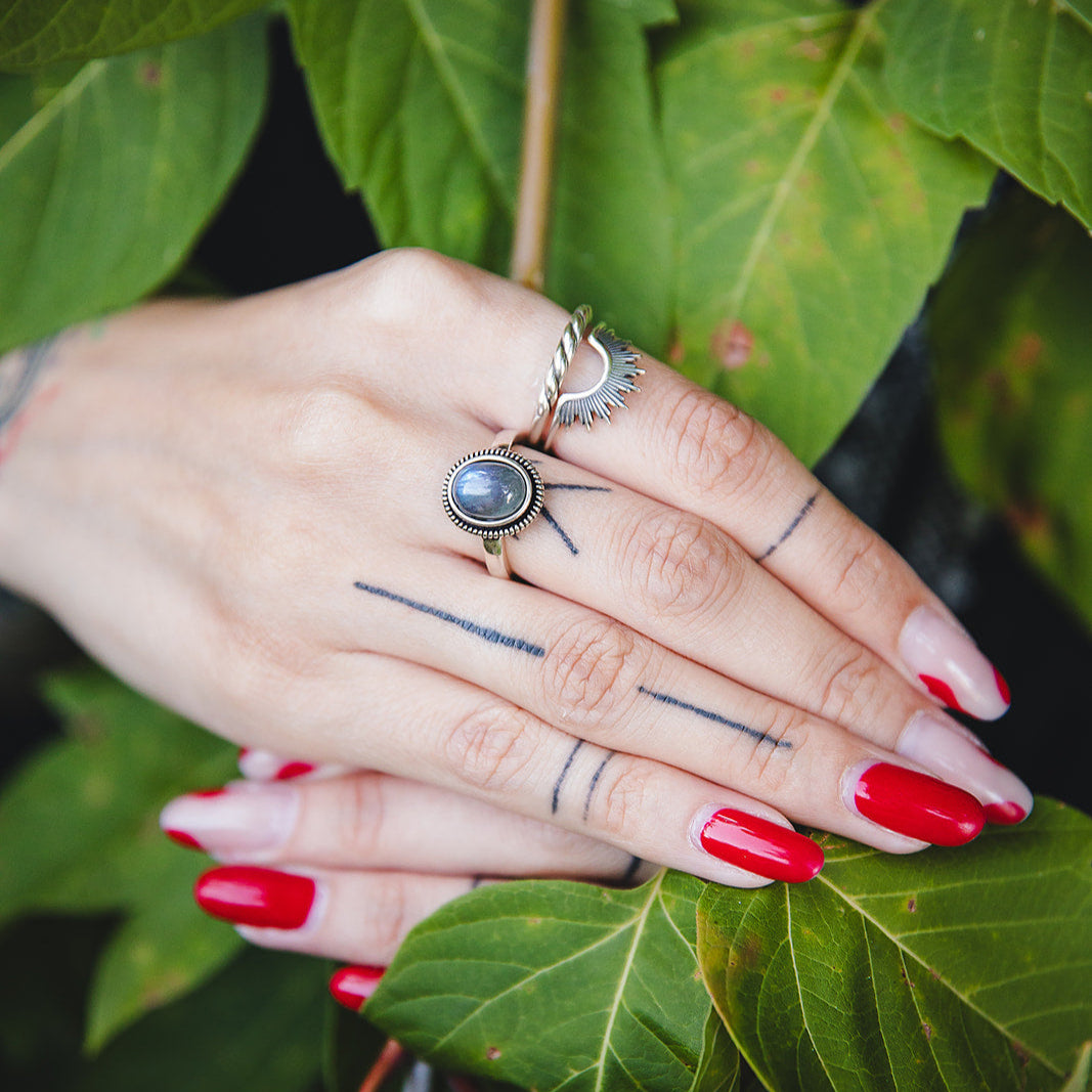 Bague torsadée Sylva en argent 925 portée à la main, mise en scène avec des feuilles vertes.