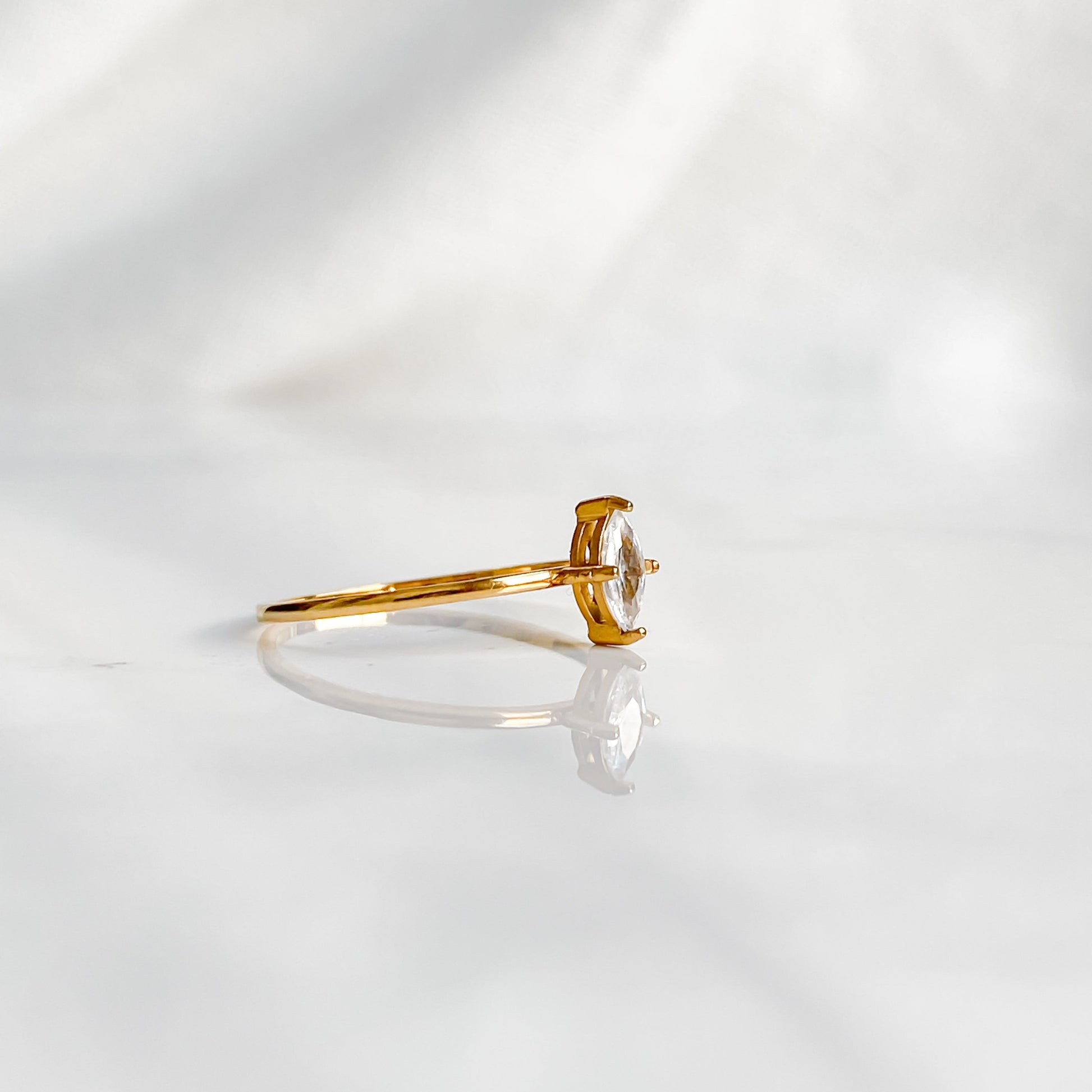 Bague solitaire dorée Venus vue latéralement, zircon marquise blanc brillant sur anneau fin.