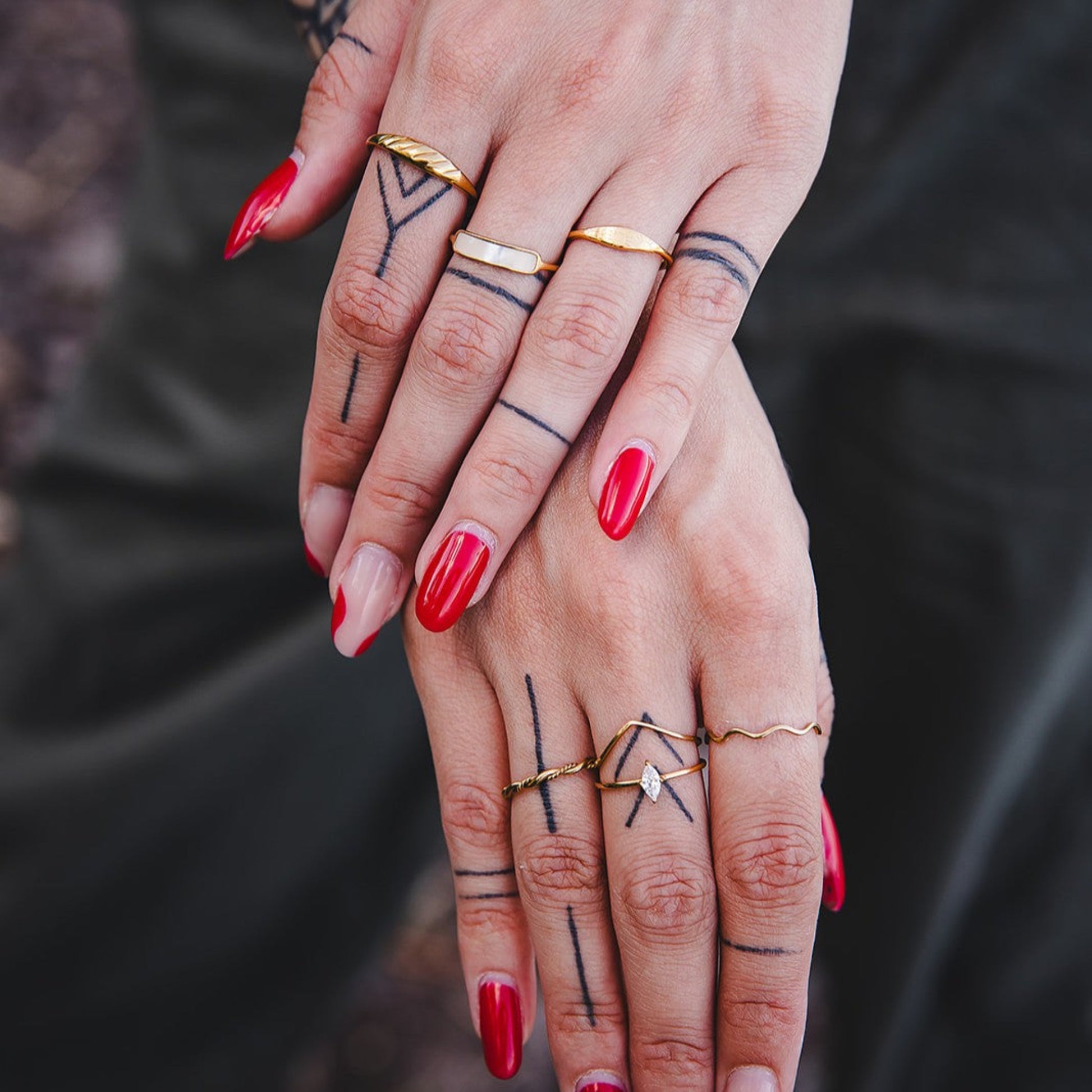 Bague Rhéa torsadée en acier inoxydable plaqué or 18K portée avec d’autres bagues dorées sur mains tatouées.