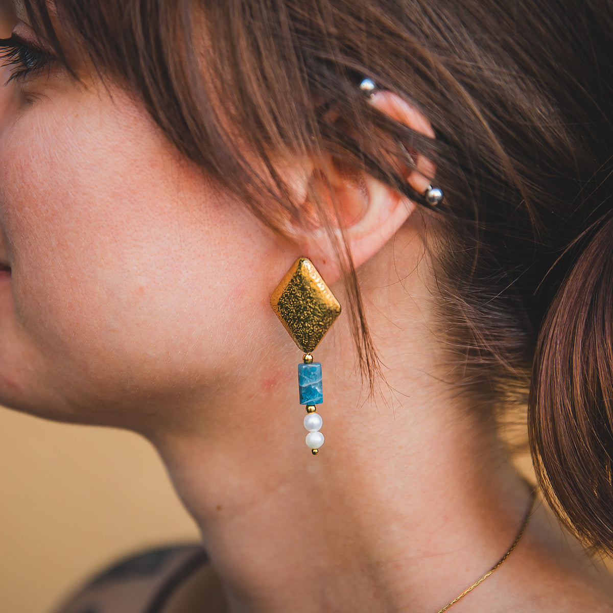 Gros plan porté de la boucle d’oreille Chaouen avec forme géométrique dorée et apatite bleue