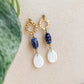 Boucles d’oreilles Abalone en flatlay sur fond beige avec feuille verte, mélange de doré, céramique bleue et nacre naturelle.