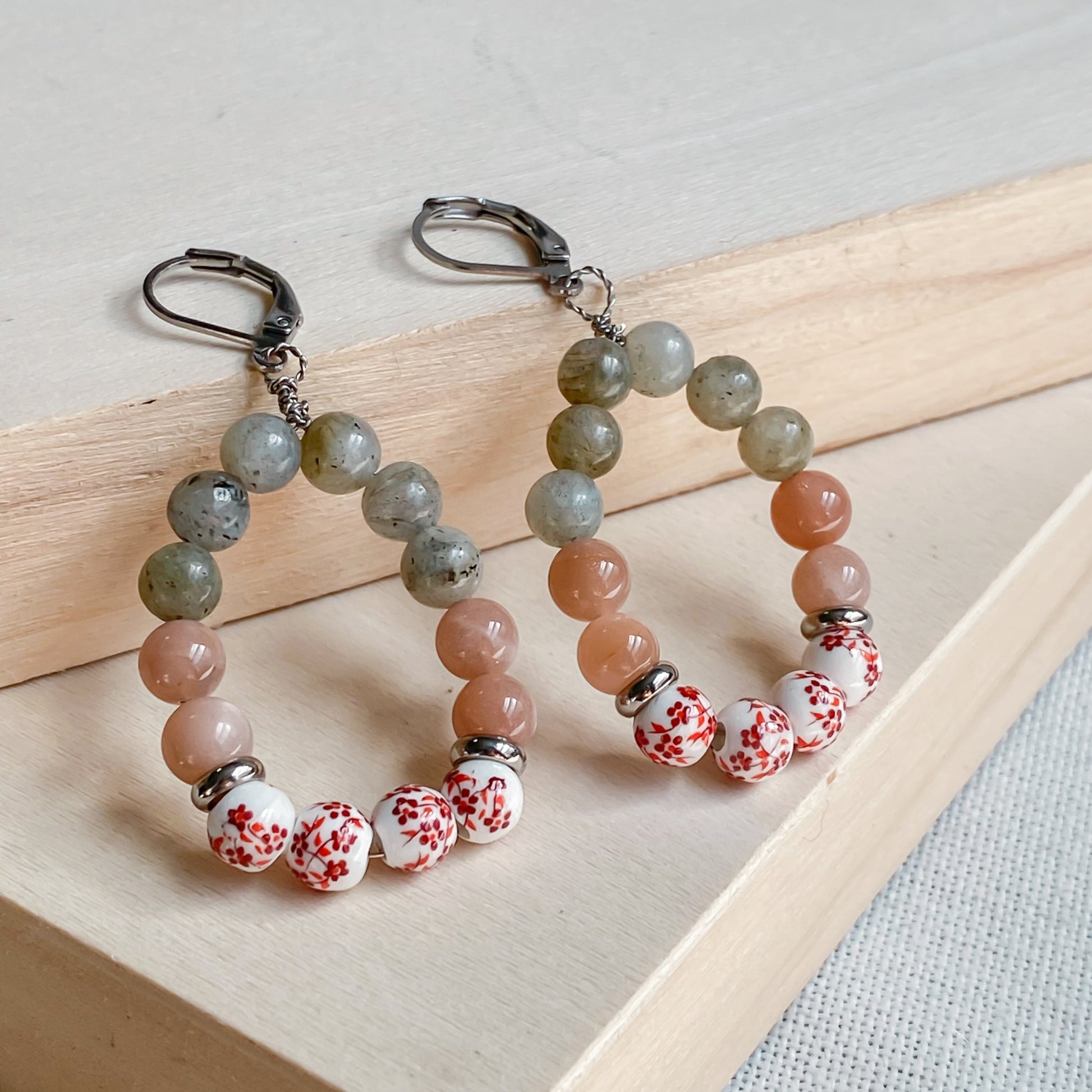 Boucles d’oreilles bohèmes en labradorite, pierre de soleil et céramique artisanale blanche à fleurs rouges – style hippie chic.