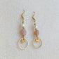 Boucles d’oreilles pendantes Daphné en plaqué or avec perles d’eau douce et pierre de soleil, photographiées en flatlay sur fond beige texturé