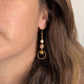Boucles pendantes Daphné en pierre de soleil et perle d’eau douce avec breloque cercle dorée, portées à l’oreille pour montrer la longueur et le style
