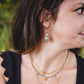 Femme portant les boucles d’oreilles Athéna en labradorite et perle d’eau douce, bijou doré 18K.