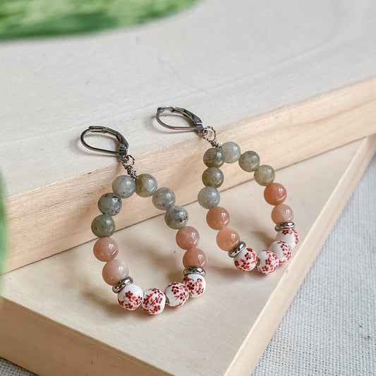Boucles d’oreilles pendantes Capri en pierres naturelles labradorite et pierre de soleil avec perles en céramique fleurie – fait main à Montréal.