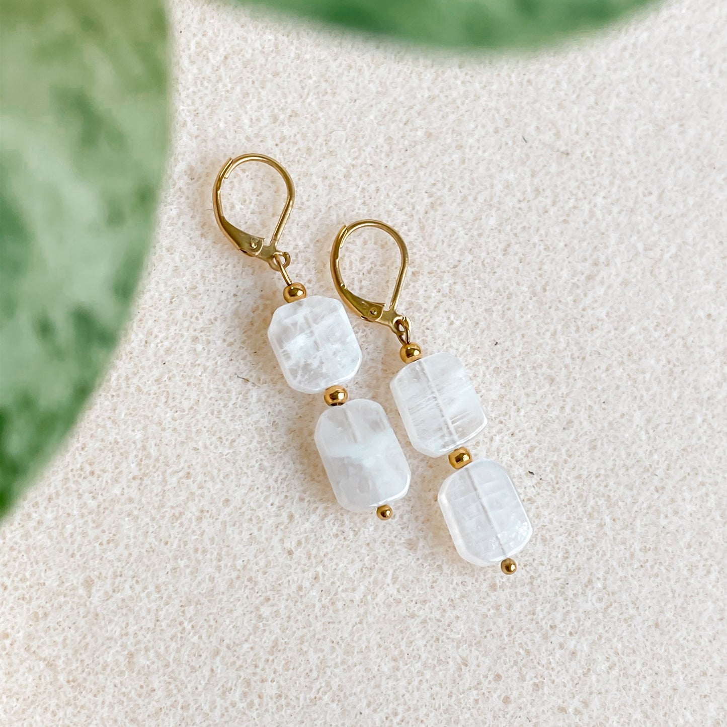 Gros plan sur les boucles d’oreilles Phoebe en pierre de lune naturelle et acier inoxydable doré, présentées à plat.