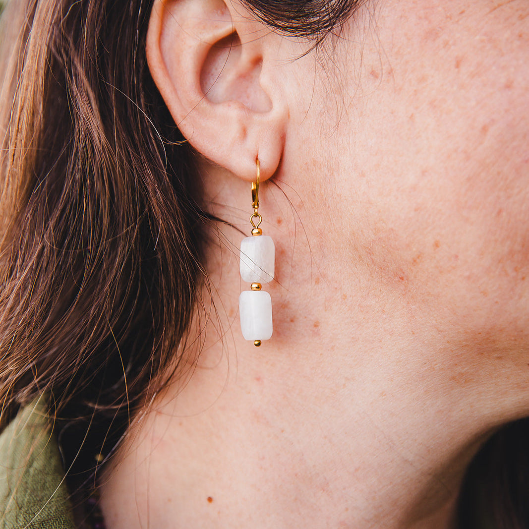 Zoom sur les boucles d’oreilles Phoebe en pierre de lune arc-en-ciel rectangulaire, montées sur acier inoxydable doré, fermoir dormeuse.