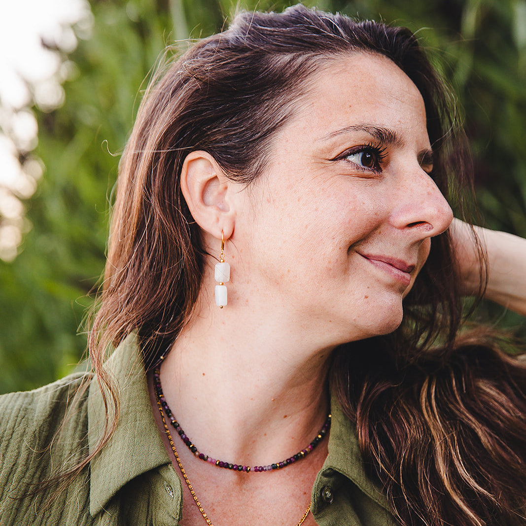 Portrait de femme portant les boucles d’oreilles Phoebe pendantes en pierre de lune et acier inoxydable doré.