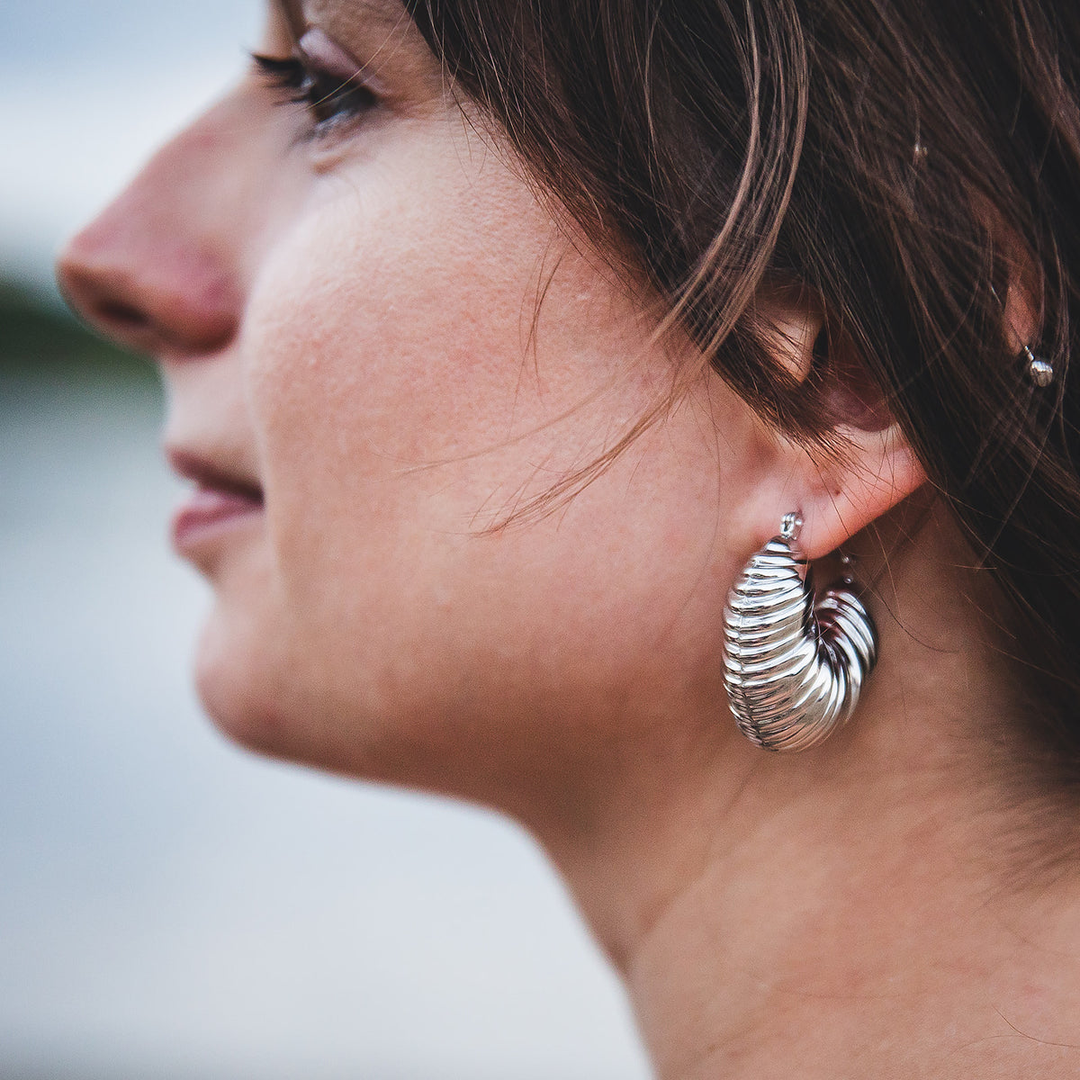 Gros plan des boucles d’oreilles Sirocco argentées portées