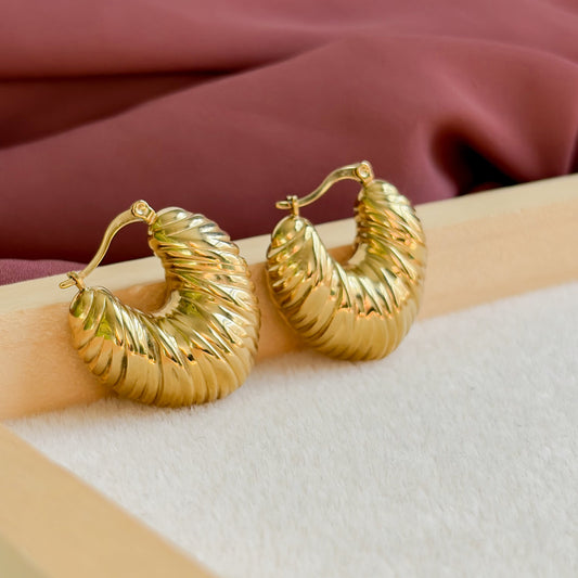 Détail de la texture ondulée des boucles d’oreilles Sirocco dorées