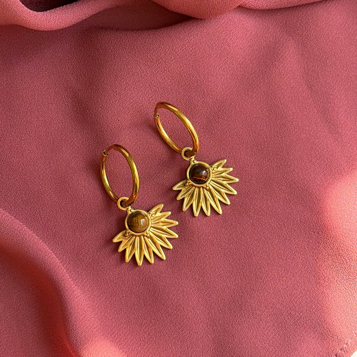 Boucles d’oreilles Zénith dorées sur un tissu terracotta