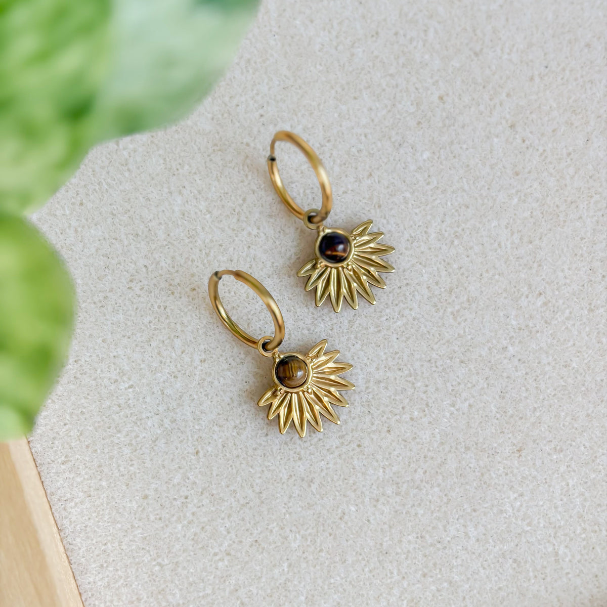 Boucles d’oreilles Zénith en œil de tigre présentées avec une feuille verte