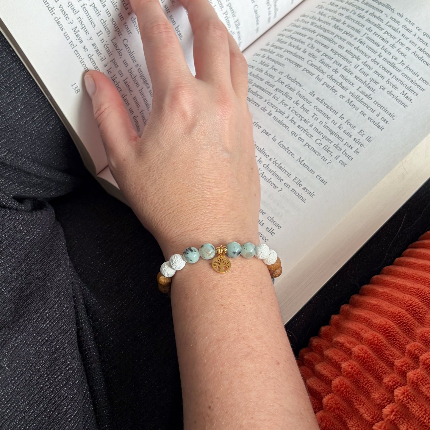 Bracelet Arbre de vie avec médaille dorée et perles vertes et blanches, porté au poignet pendant une pause lecture.
