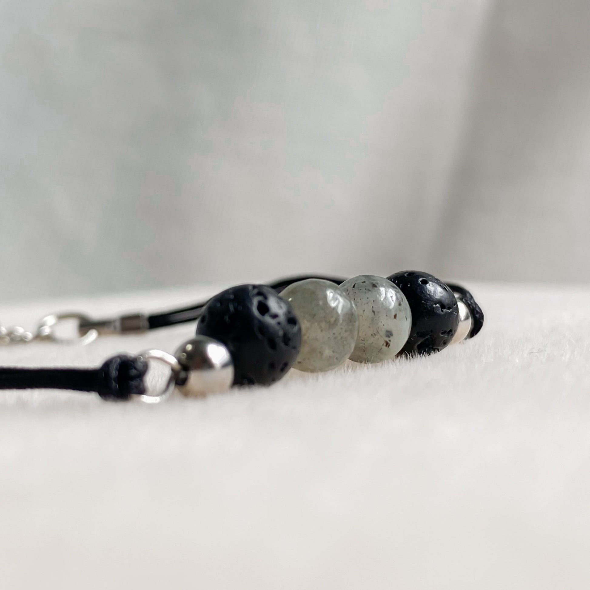 Gros plan sur un bracelet artisanal en pierres de lave et labradorite de 6 mm, monté sur cordon noir avec détails en acier inoxydable.