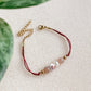 Bracelet cordon rouge vin ajustable Éveil avec pierre de soleil, perle d’eau douce et céramique fleurie, fermoir mousqueton doré et chaîne d’extension.