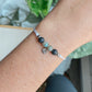 Bracelet cordon personnalisable Doux Souvenir porté au poignet, en inox argenté avec des pierres de lave et de labradorite, accompagné d'une breloque.