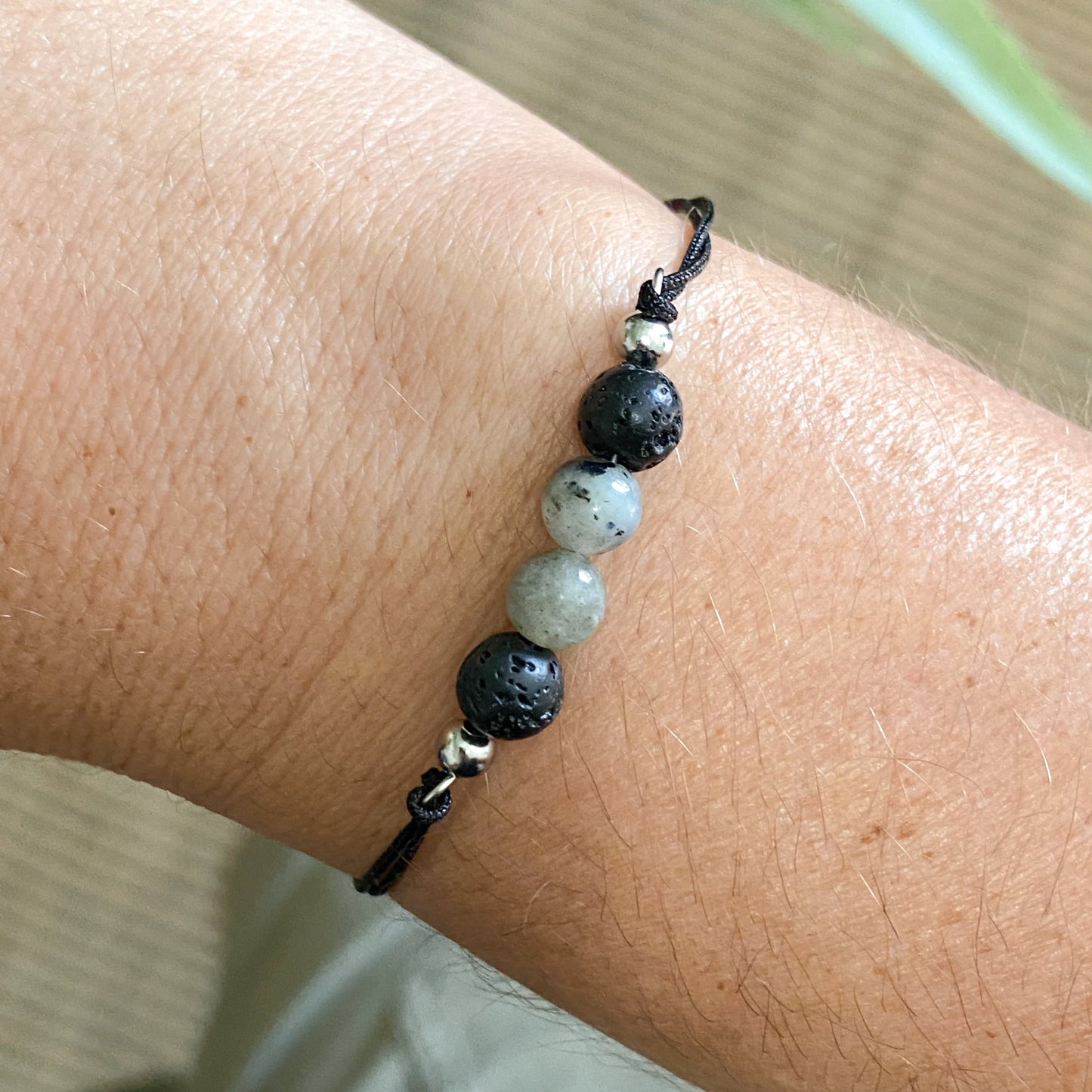 Gros plan sur un bracelet cordon noir avec perles en pierre de lave et labradorite naturelles de 6 mm porté sur le poignet.